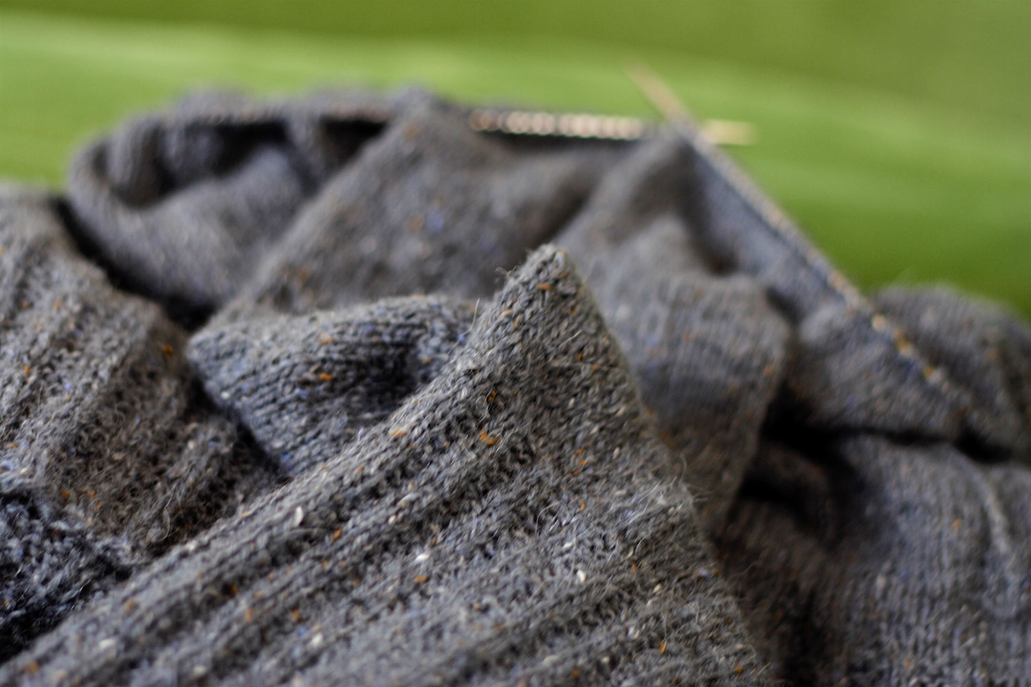 Grey knitting project sitting in a heap; garter ribbing in the foreground and the needles are out of focus in the background.