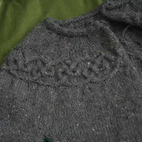 Neckline and one shoulder of circular yoke cardigan with cabled motif rounding around shoulders.