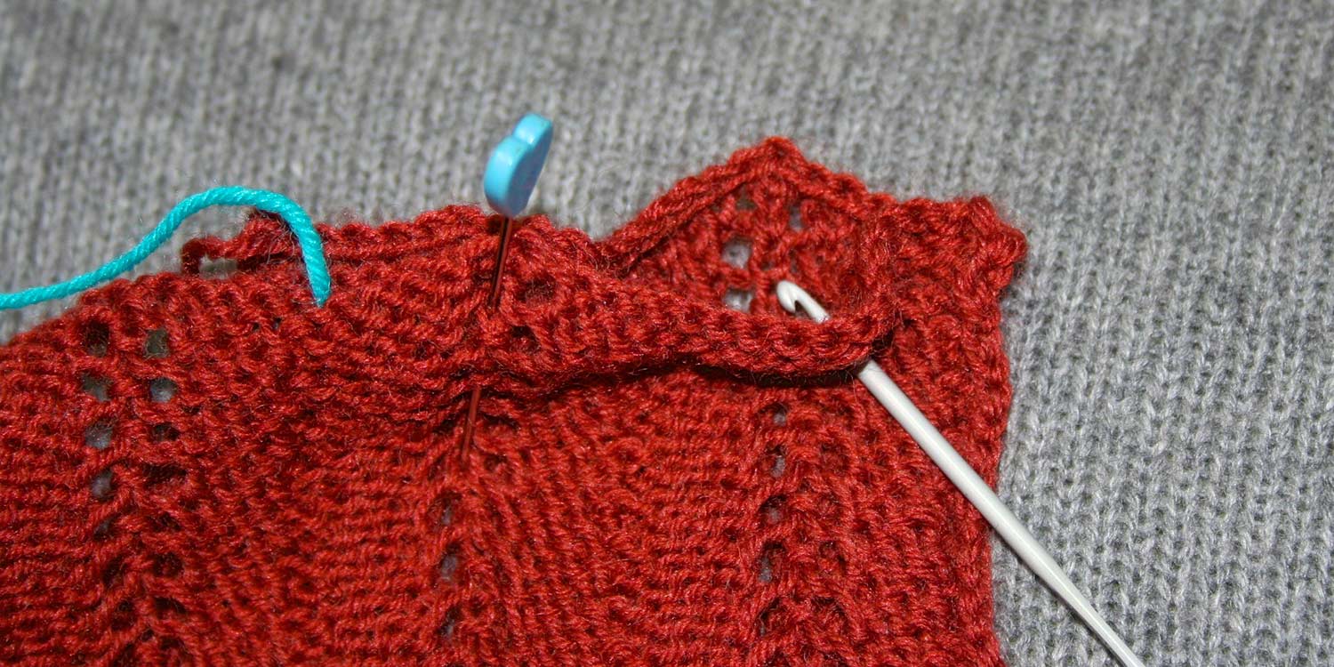 Two pieces of knitting pinned together but seam allowance opened up to show crochet hook about to go through back piece in same location as it when through the front piece.