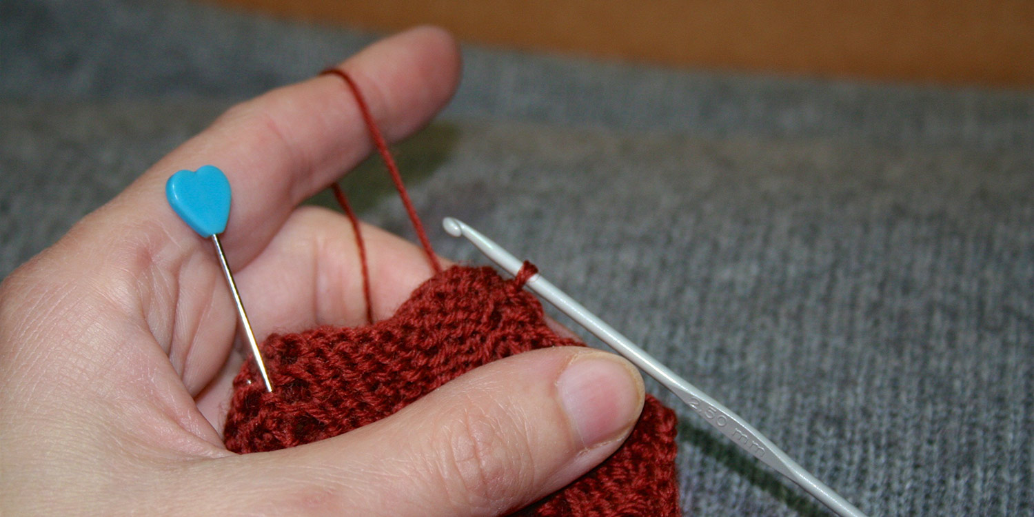 Left hand holding knitting and tensioning yarn for crochet hook that's being used for seam.