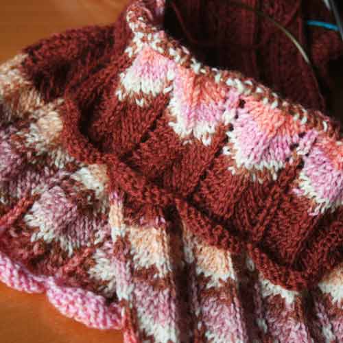 Pieces of knitting in progress worked in self-patterning yarn in pinks, corals and white and a solid colour in rust.