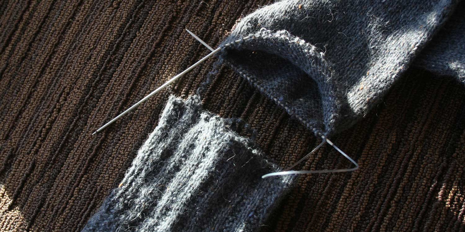 Sweater sleeve on a circular needle with the separated sleeve cuff sitting next to it.