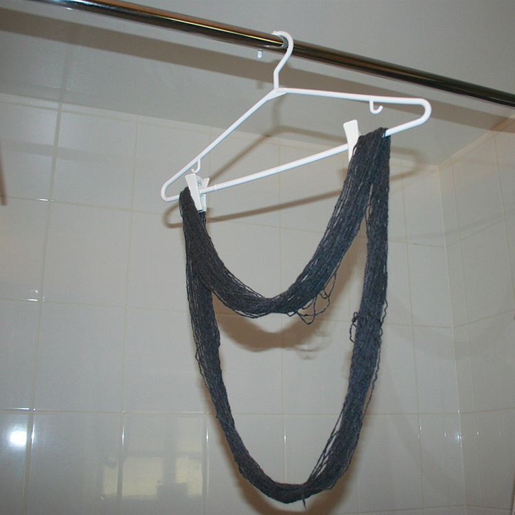 Skinny skein hanging from a white hanger on a shower rod.