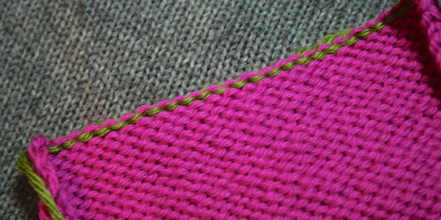 Wrong side of pink knitting showing what looks like green purl bumps at top edge.
