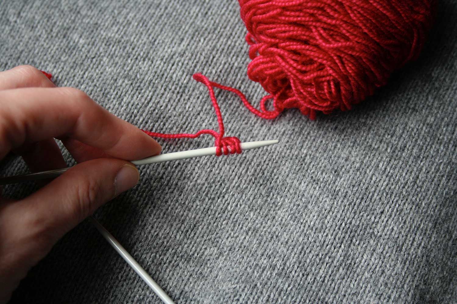 Left hand holding needle with cast on and stitches are near right side of needle, with right side facing and working yarn coming from stitch furthest from needle tip.
