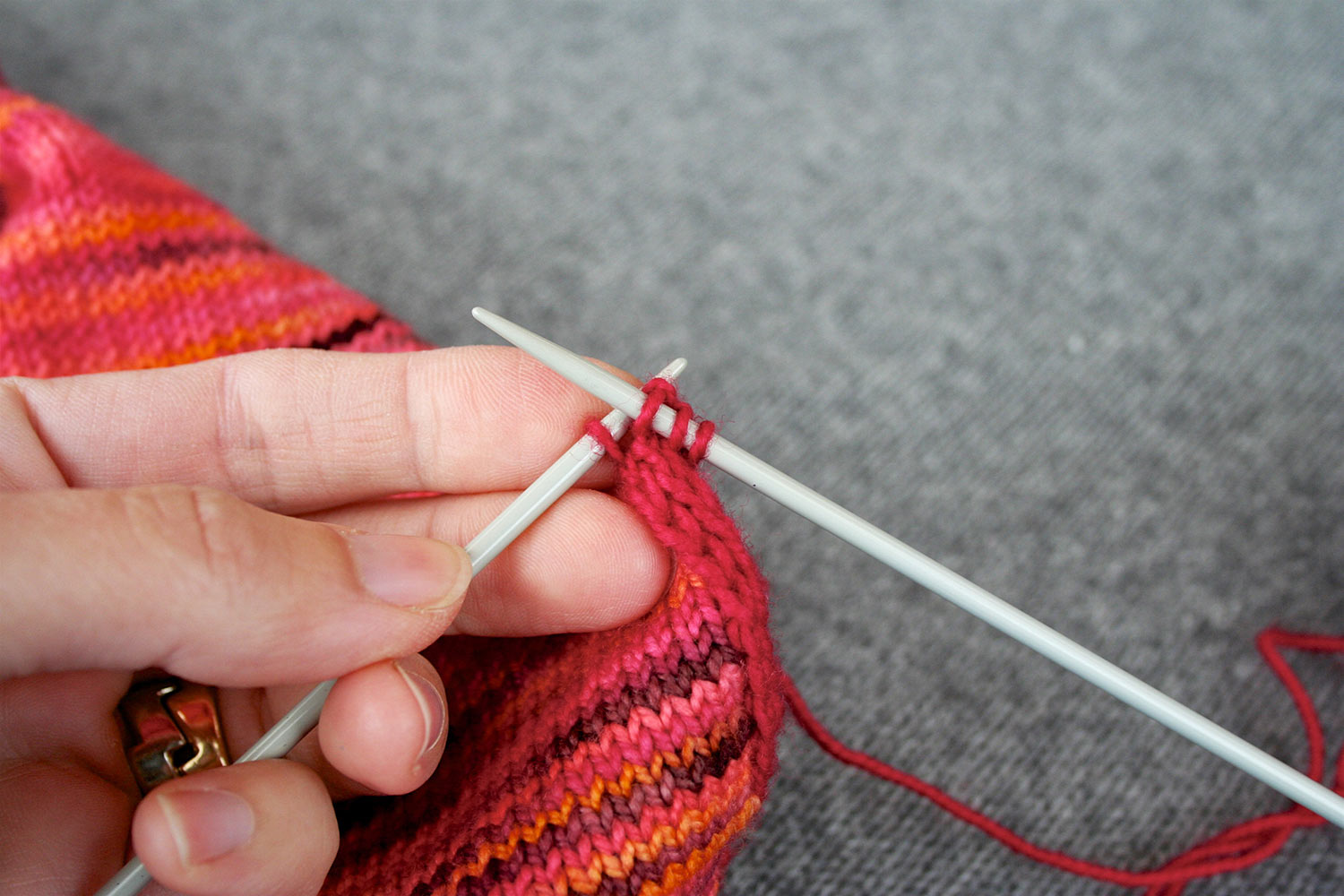 Three stitches on right needle and fourth stitch on left needle; below needles the applied i-cord can be seen along the edge of a piece of knitting.