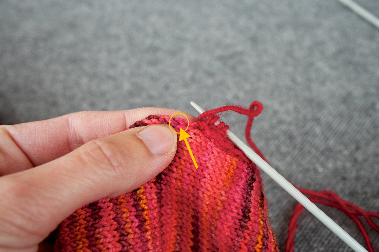 Left hand holding selvedge edge of knitting while right needle has four stitches and yarn has been brought to the front; yellow arrow and circle indicate location to insert needle.