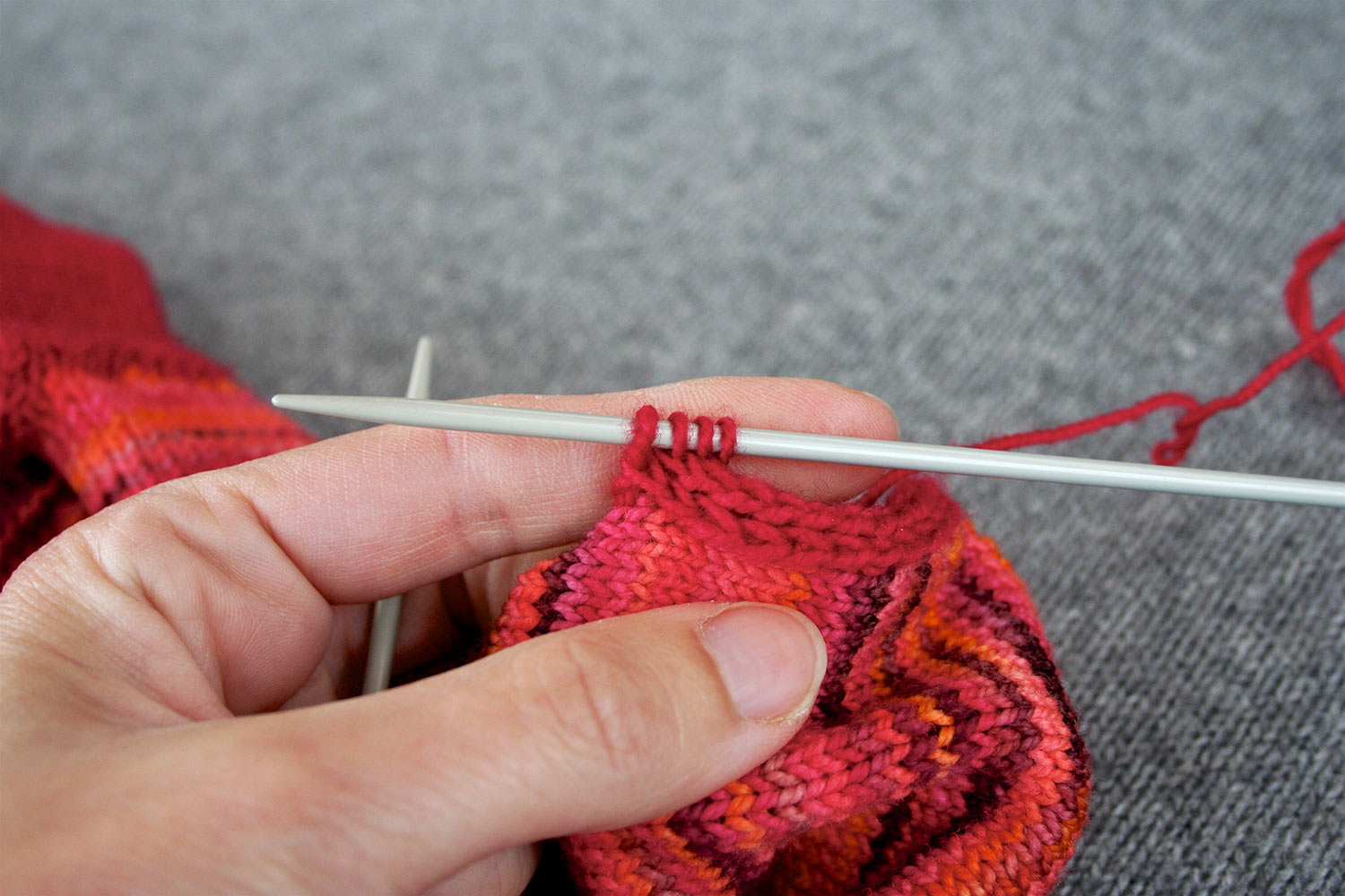 Left hand holding up knitting and showing four stitches on right needle.