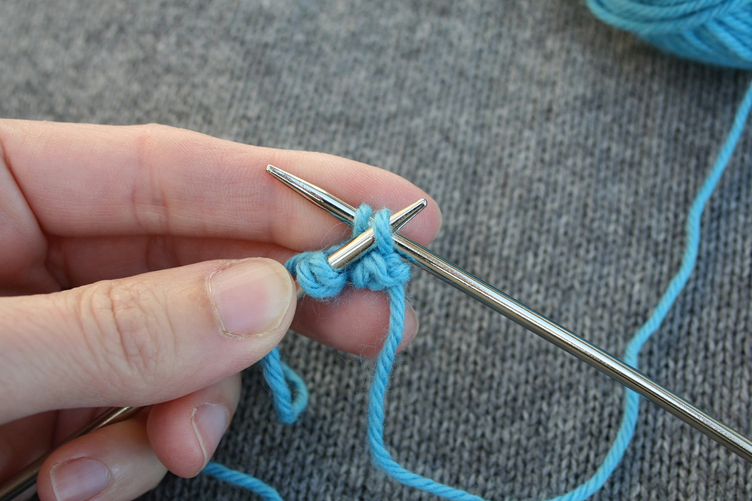 Left needle is inserted into second stitch from end of right needle, preparing to pass it over last stitch in a bind off.