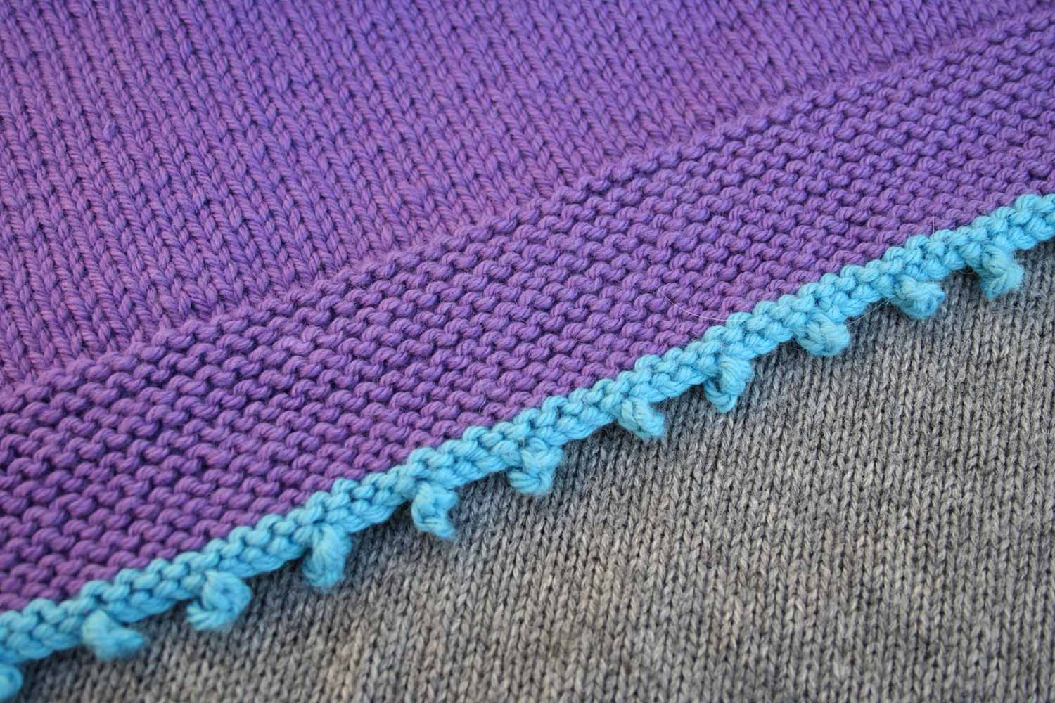 Blue picot cast on with four stitches between them and a garter stitch ridge above it, followed put a wide band of purple garter stitch and then stocking stitch.