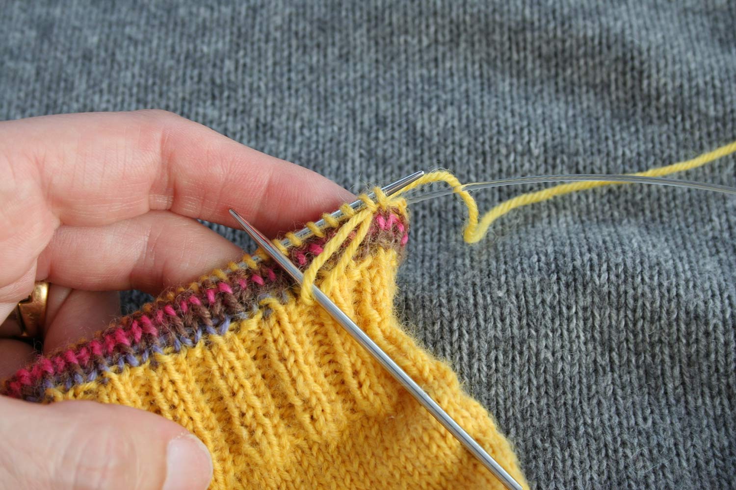 A large loop of yarn being drawn through the first two stitches on the left needle.