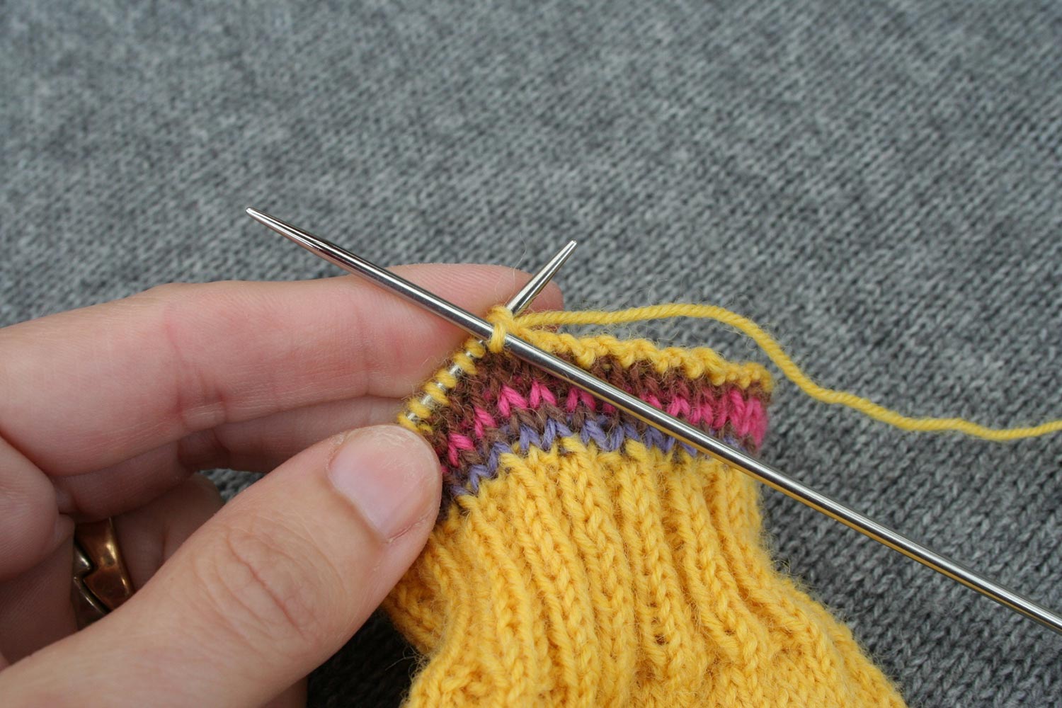 Bind off being worked on a sock cuff with right needle performing a knit two together (k2tog).