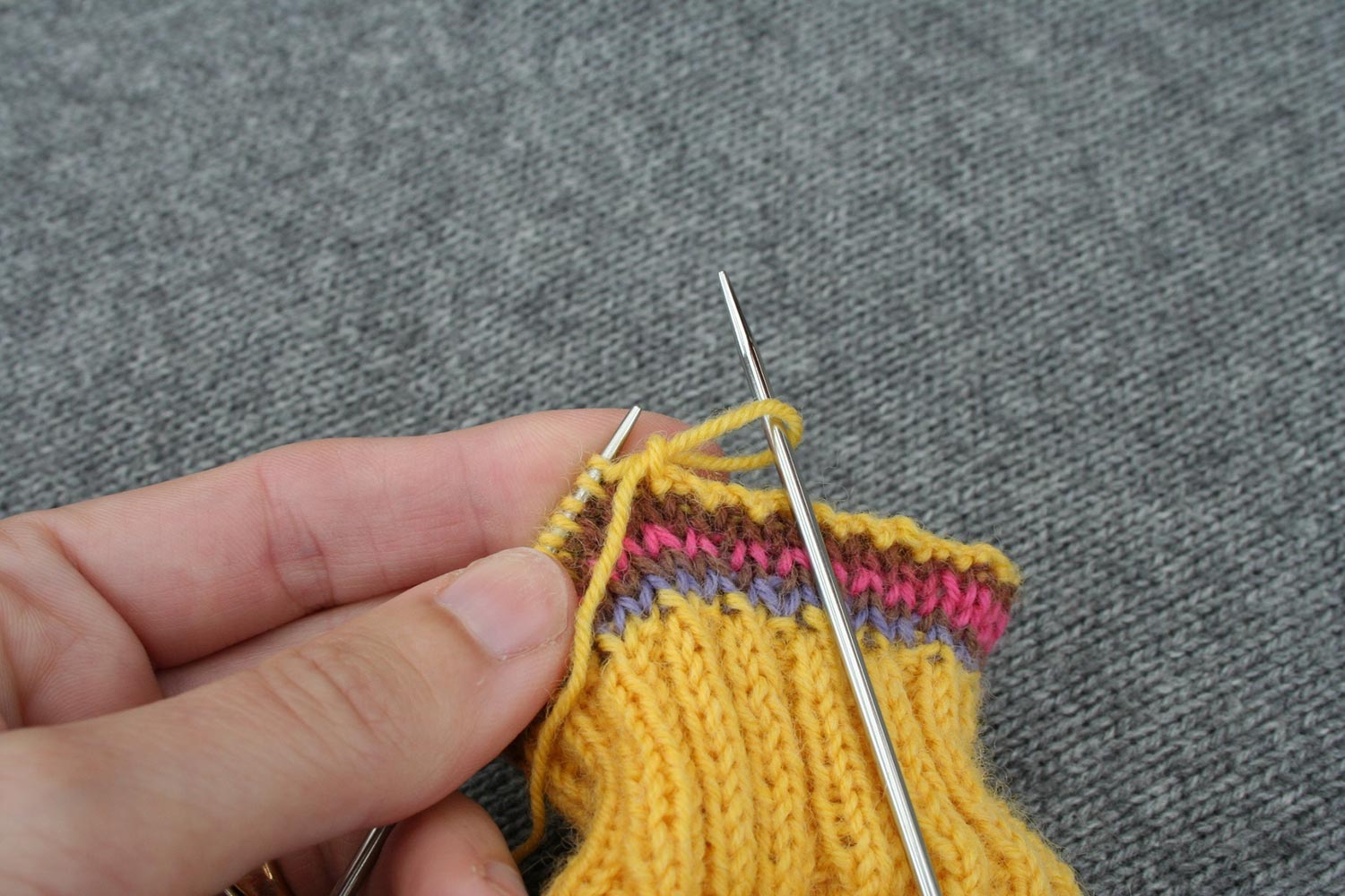 Needle pulling on the only stitch on right needle to enlarge it and pull the tail through.