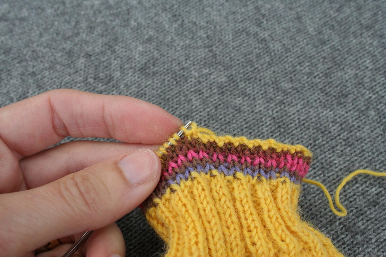 Two step repeat of bind off completed showing tail threaded through first stitch on left needle, then last stitch worked that has just been slipped off needle.