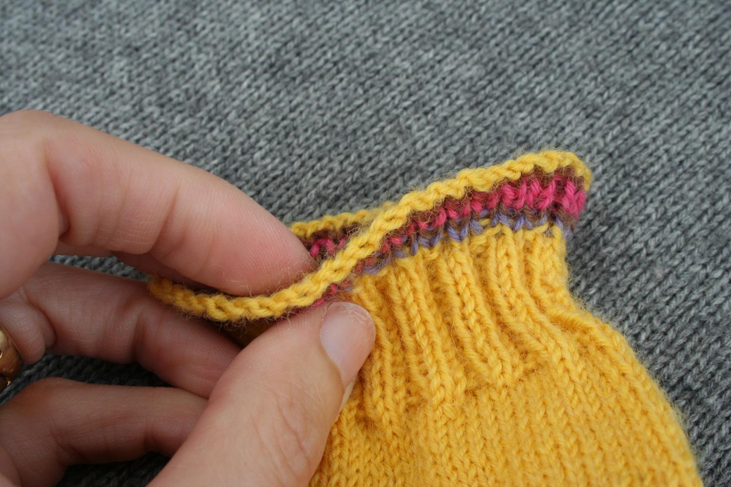 Bind off edge of cuff held between thumb and finger and bent towards camera for bird's eye view of top of bind off.