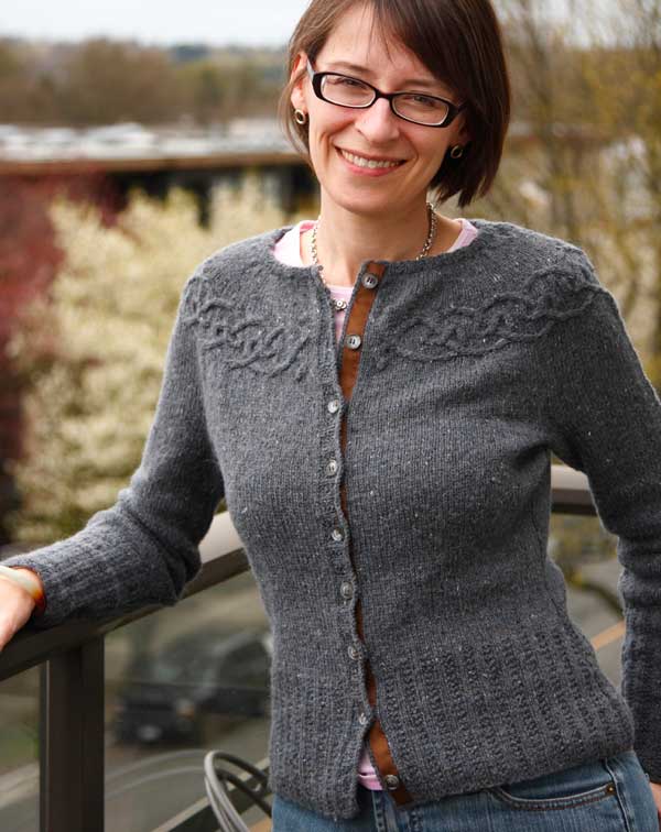 Holli wearing a grey cardigan with cables around the yoke and a brown gros grain ribbon on the button band.
