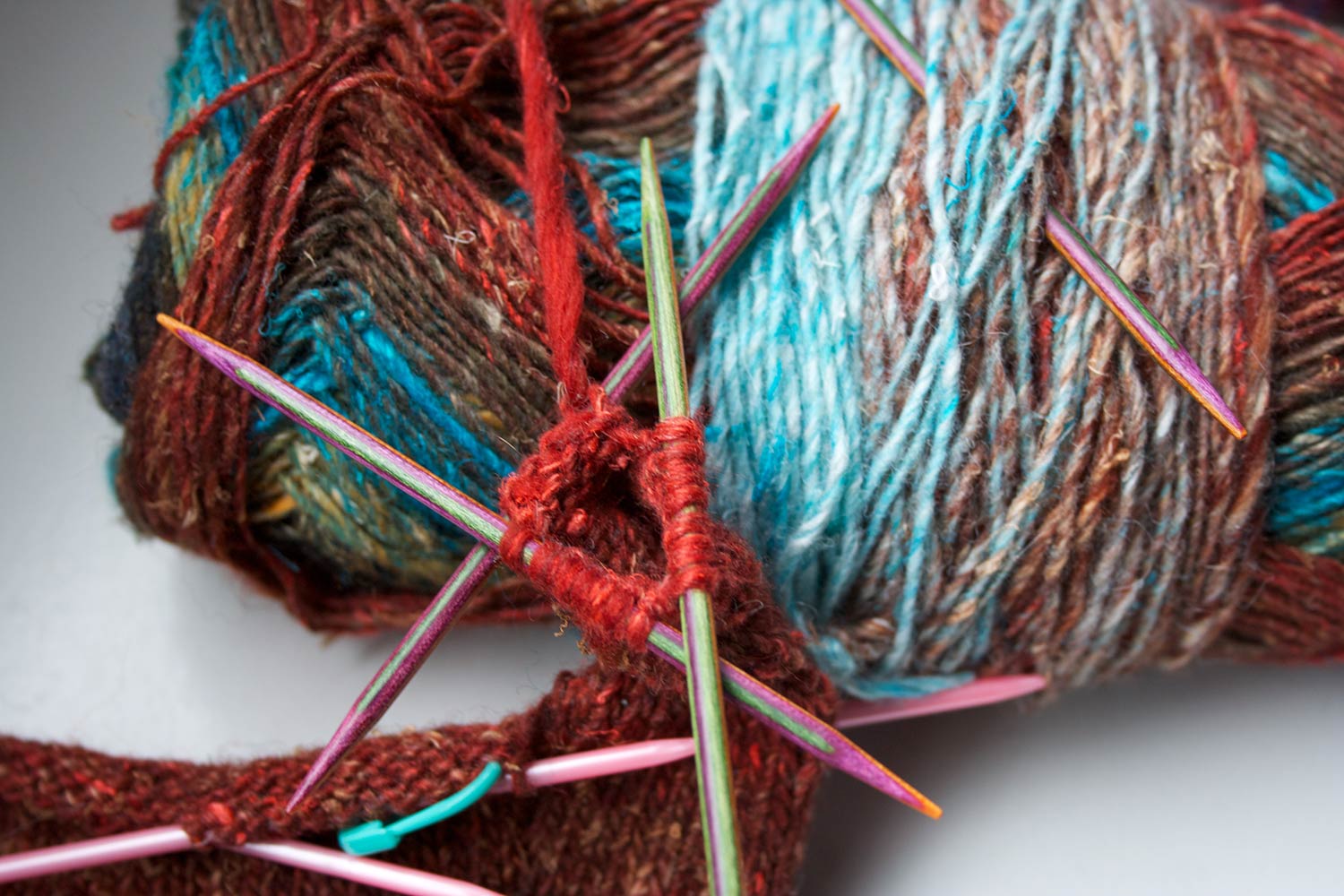Stitches on three double pointed needles and finger partially knit, leaning agains a ball of yarn.