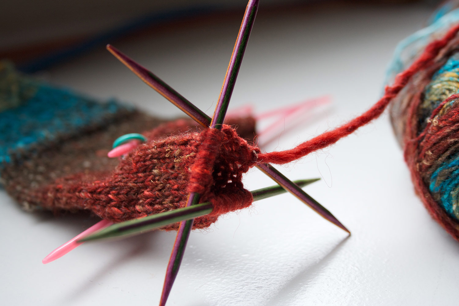 Three double pointed needles with a knitted finger extending behind them, propped up on a white surface.