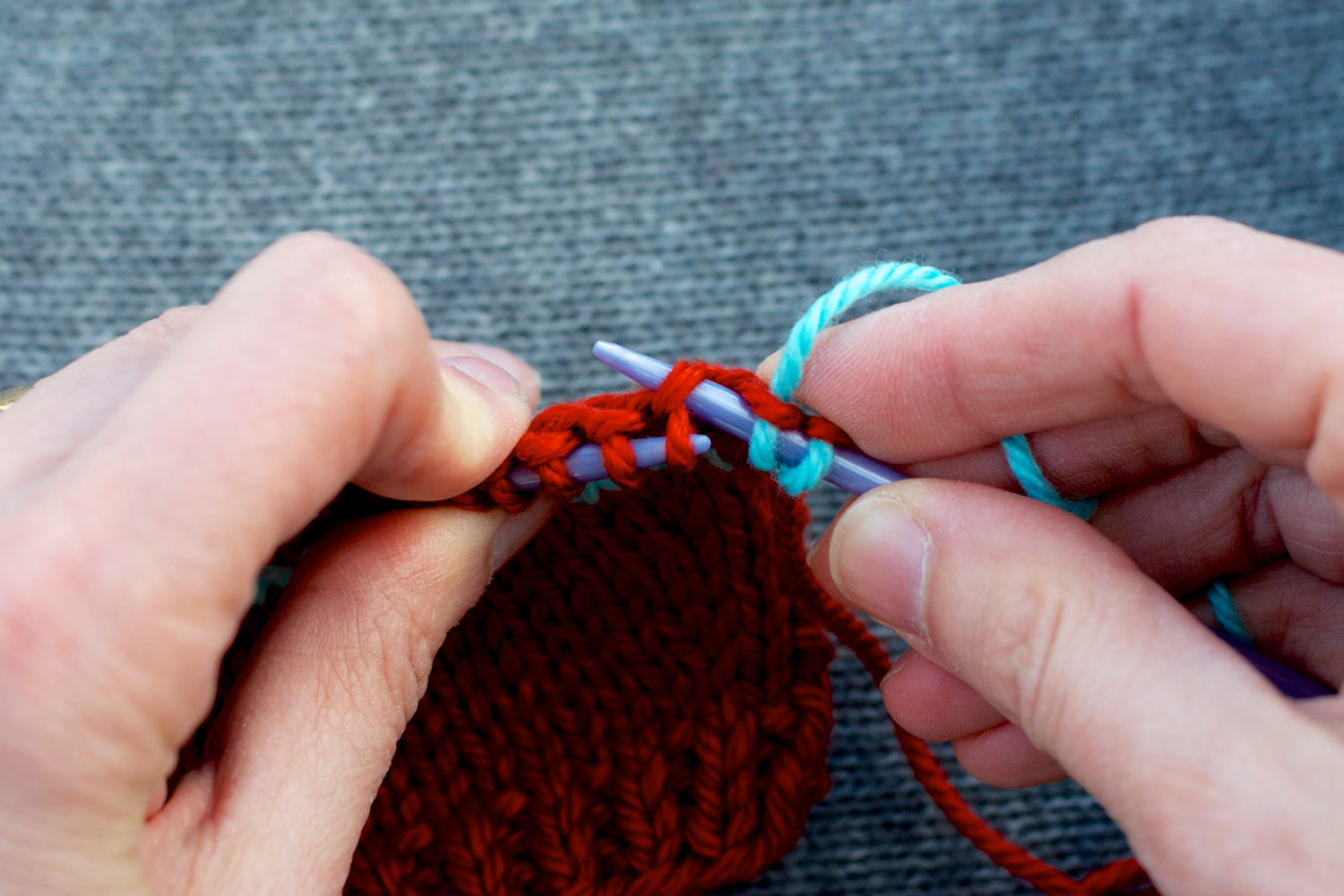 Right needle inserted into purl bump at back of left needle, one row below the stitches on the needle.
