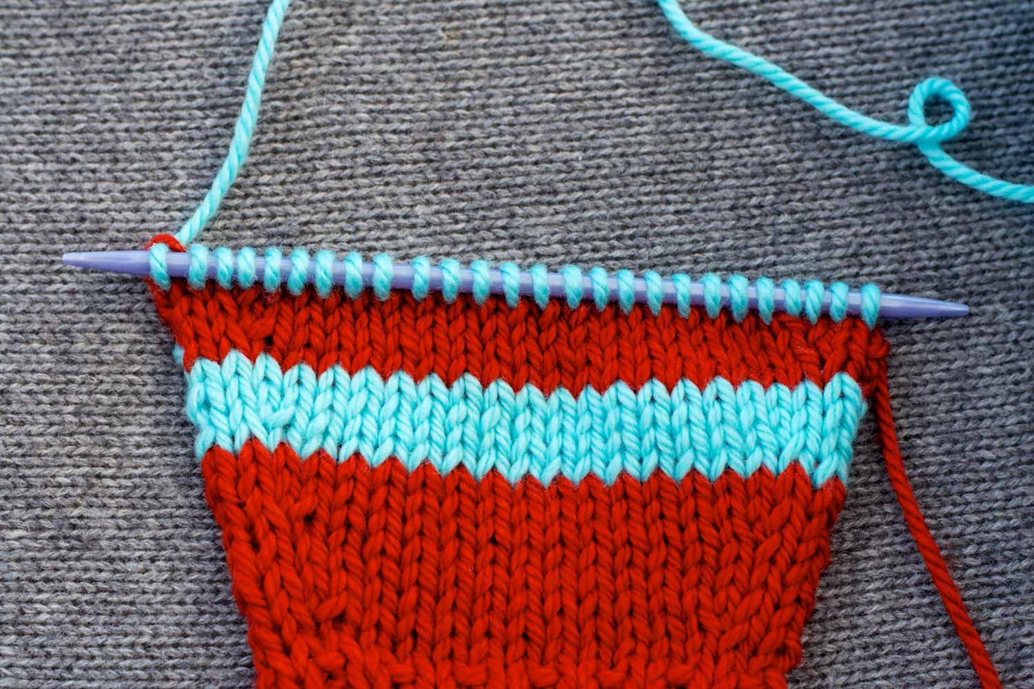 Striped swatch on the needles with mirrored raised increases near each edge .
