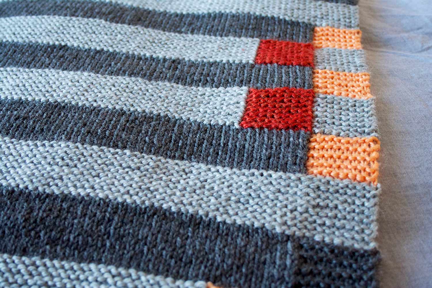 Detail shot of a two-tone grey, garter stitch blanket with rust and peach squares.