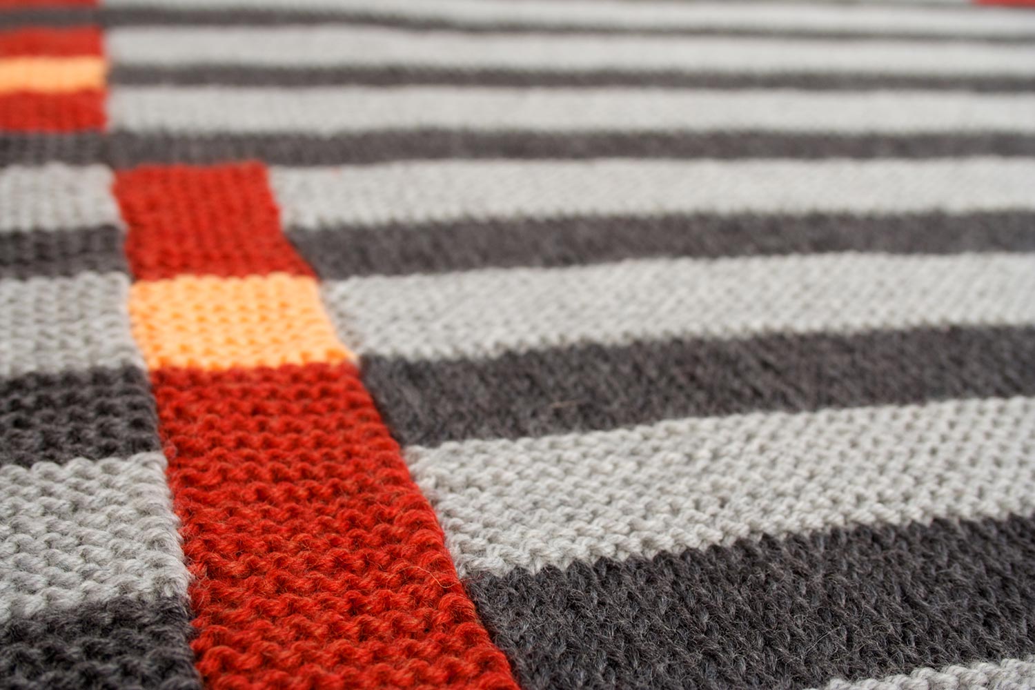 Detail shot of a two-tone grey, garter stitch blanket with rust and peach blocks.