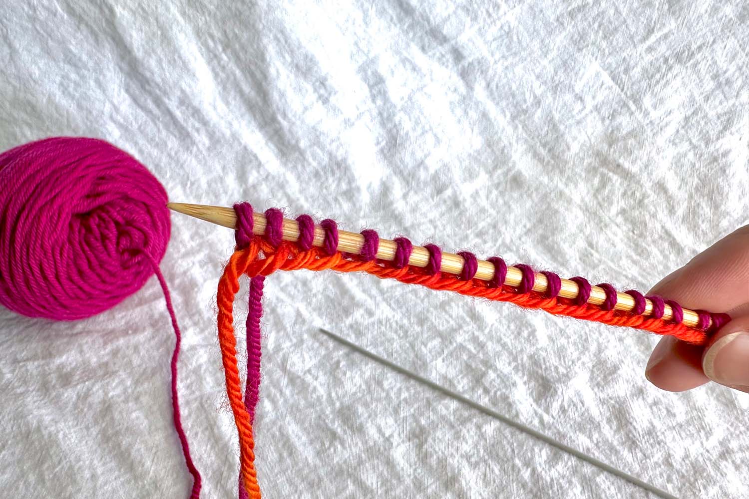 Finished cast on shows several stitches on needle and evenly spaced; second smaller needle has been removed from stitches and is sitting on table.