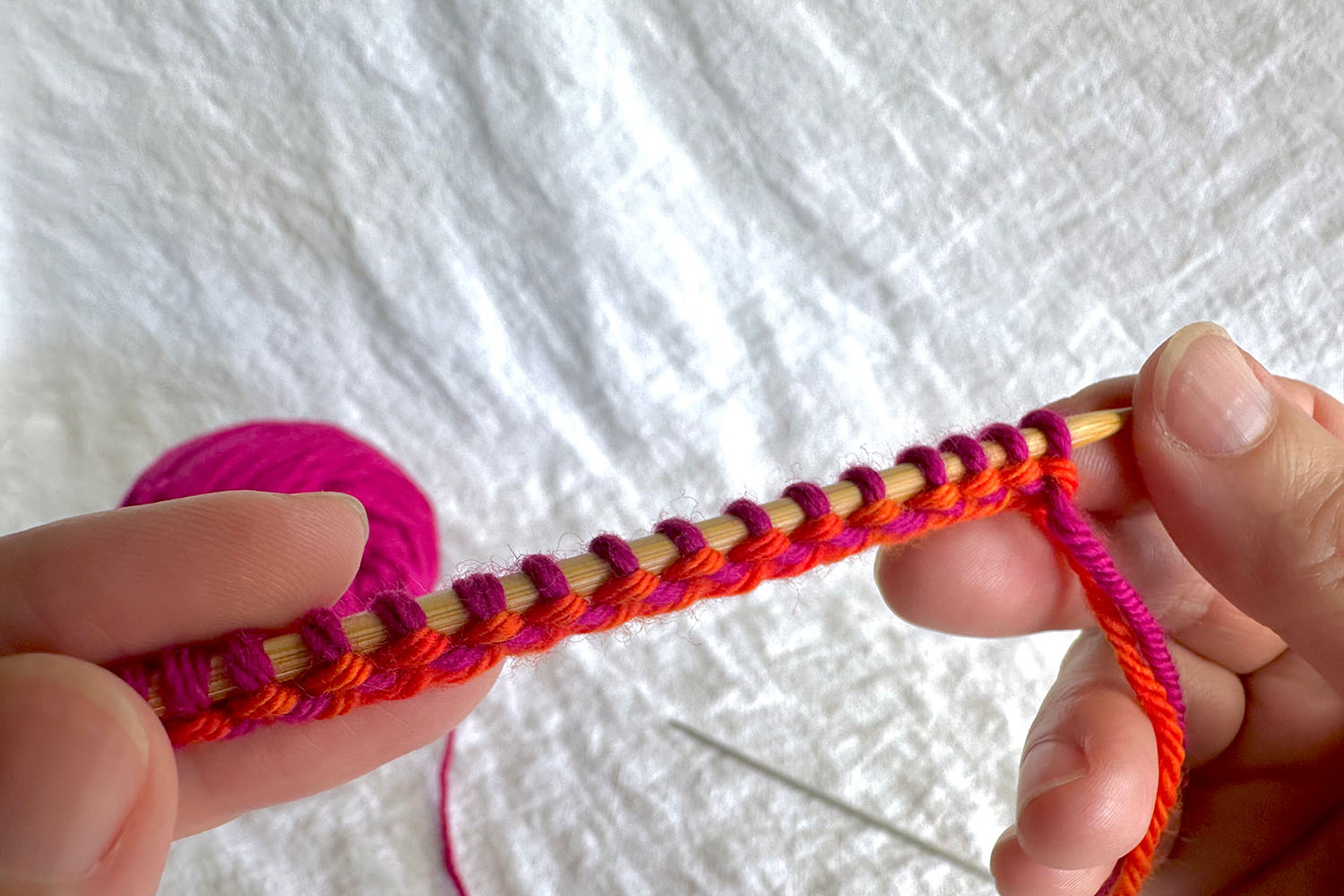 Wrong side of finished cast on shows several stitches on needle and evenly spaced and purl bumps of wrong side showing; second smaller needle has been removed from stitches and is sitting on table.