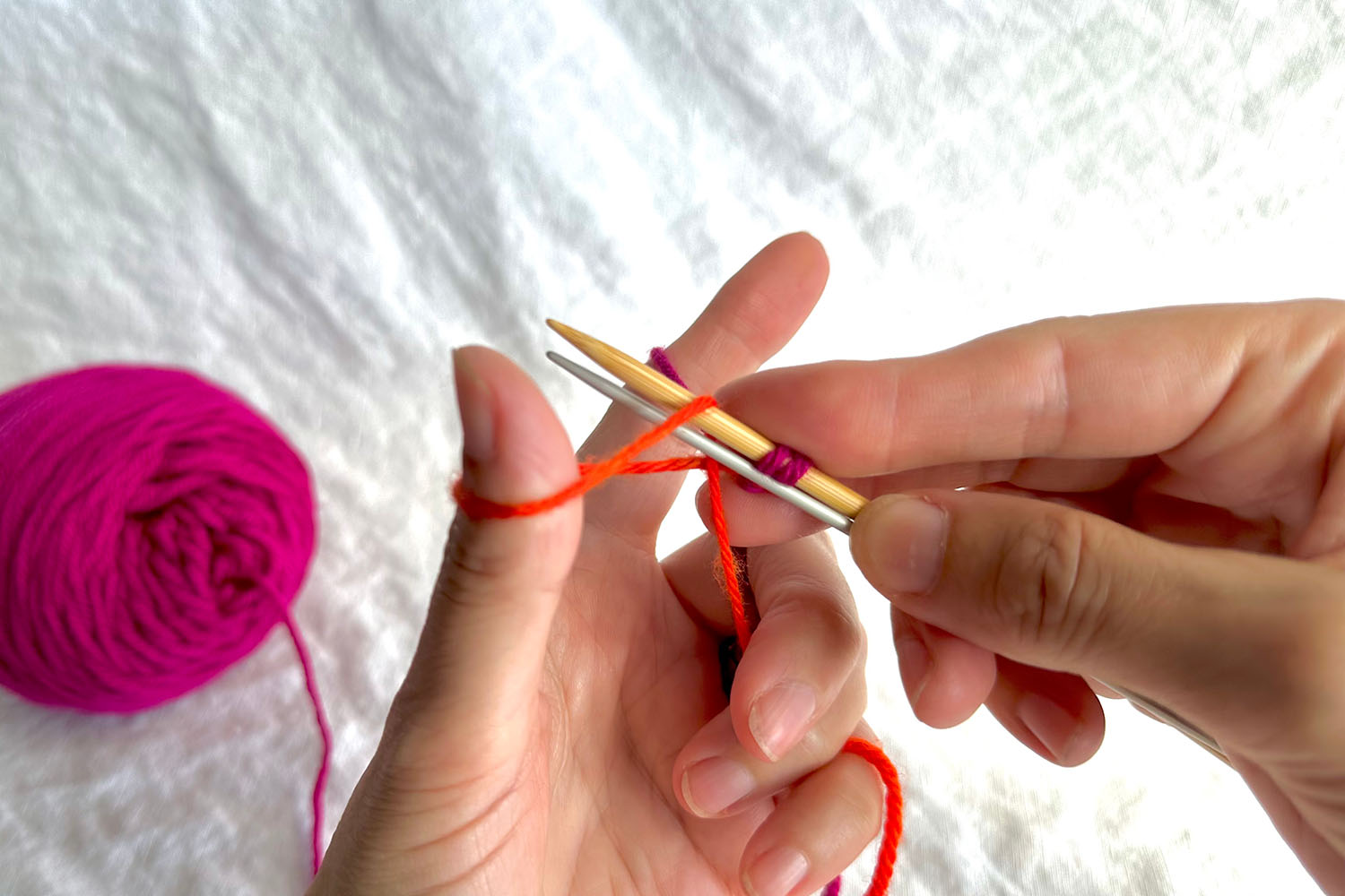Both needles of Double Needle Cast On are inserted through thumb loop.