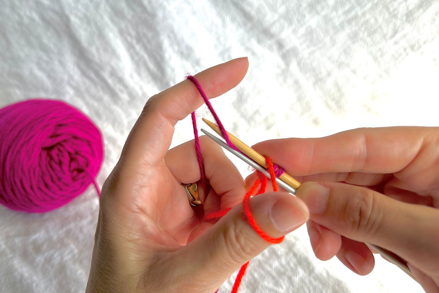 Near strand of finger yarn is wrapped around larger needle from back to front between the two needles.