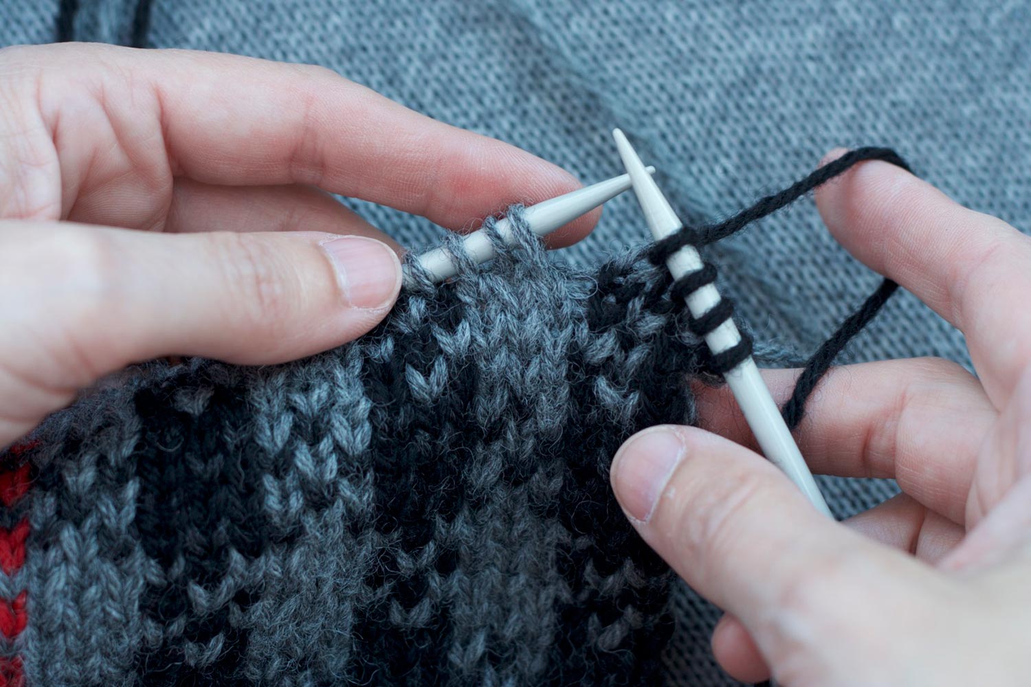 Two hands knitting with black stitches on right needle and grey stitches on left needle.