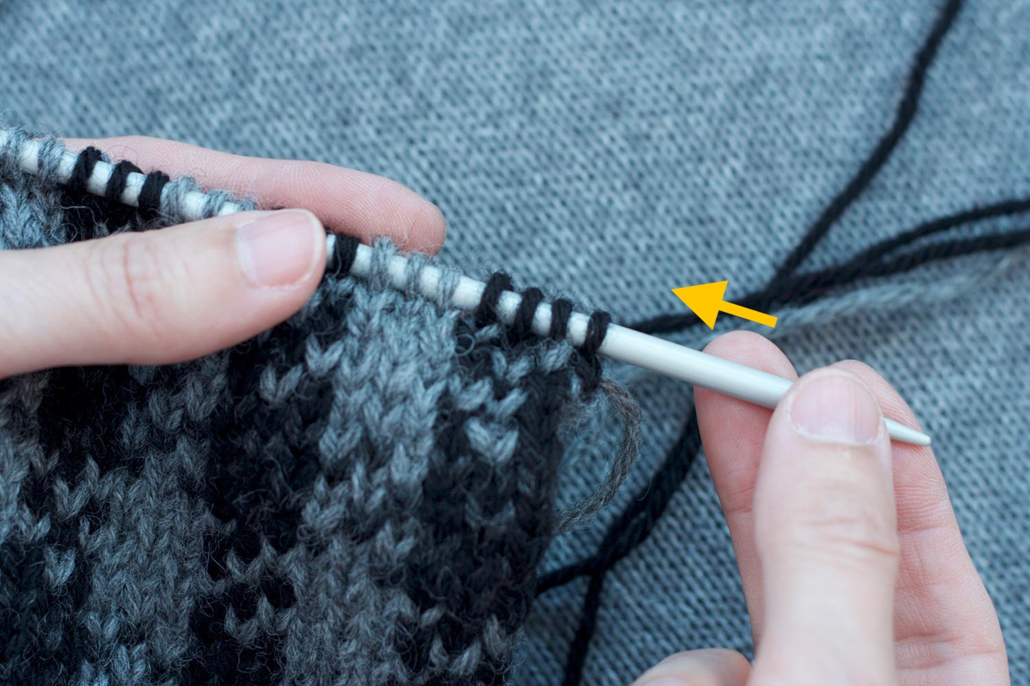 Left hand holding stitches on needle with right side facing; a yellow arrow indicates the right hand is pushing the needle to the left allowing the stitches on the needle to slide to the other end.