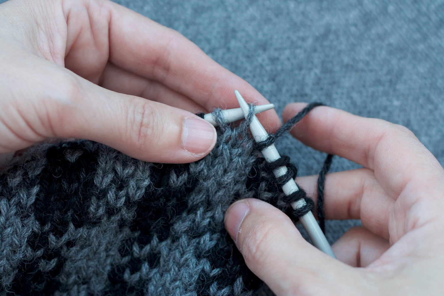 Hands holding knitting on the needles and showing the right needle is slipped into the next stitch on left needle, slipping it purl wise.