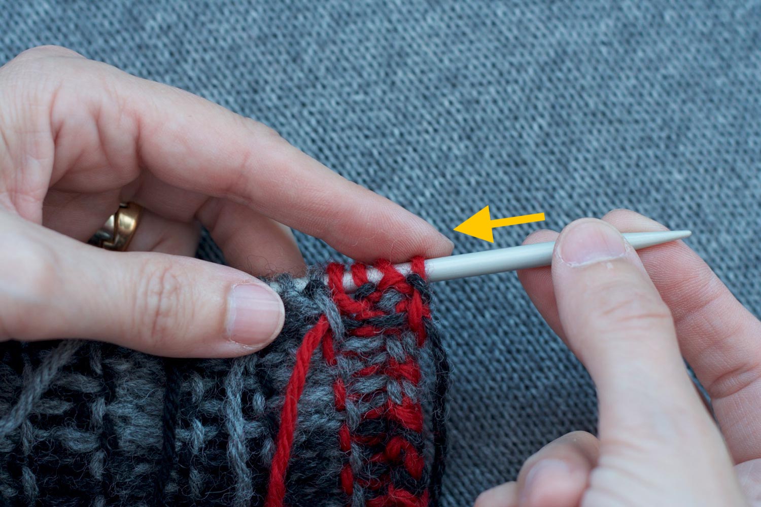 Stitches on the needle with the wrong side facing and held in left hand; yellow arrow points to the left indicating direction right hand is pushing needle.
