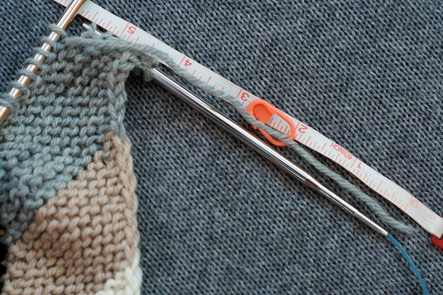 5 ½" tail with a measuring tape laid alongside it; stitch marker pinned at the 2" mark; tail extends from last st worked which is 6 stitches from end of row.