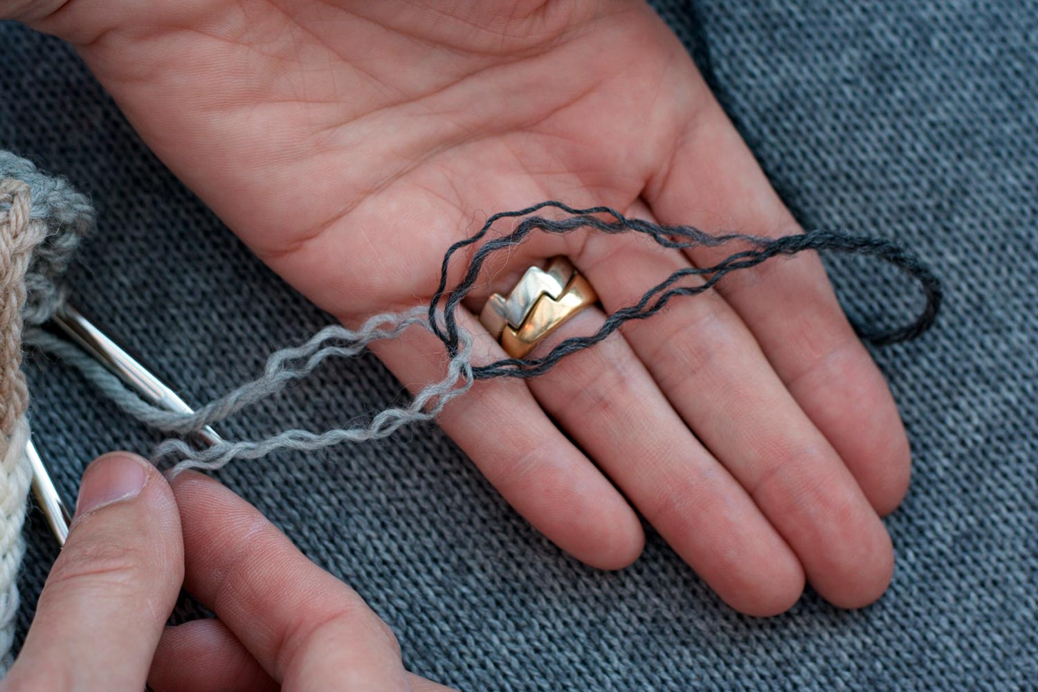 Unplied ends of two different colours of yarn looped through one another and laid across fingers of a face up palm.