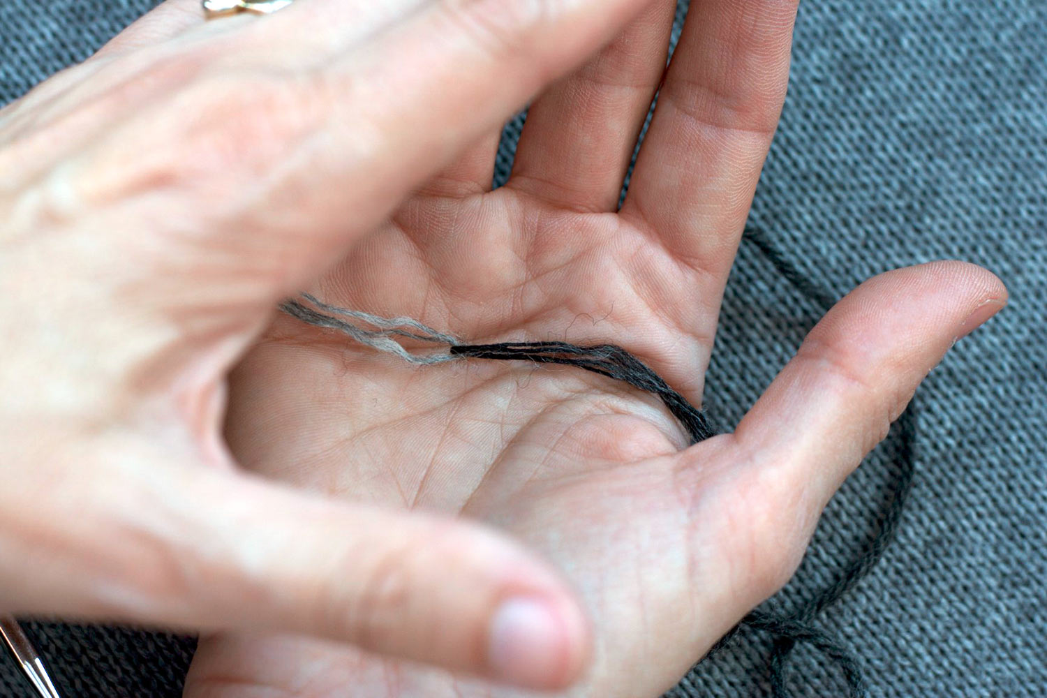 Wet ends of yarn looped around one another laid across palm with other hand about to sandwich the yarn.