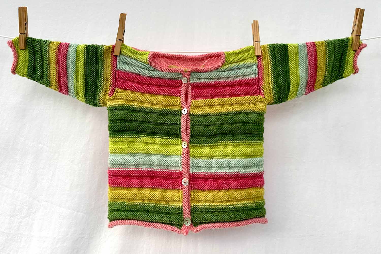 Baby cardigan with ridged texture in self-striping yarn hanging on clothes line.