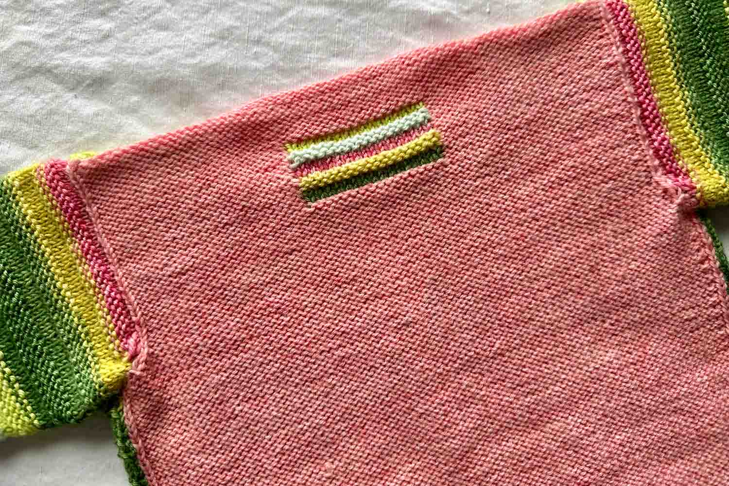 Back detail view of baby cardigan in Reverse Stocking Stitch with striped intarsia rectangle near back neck.