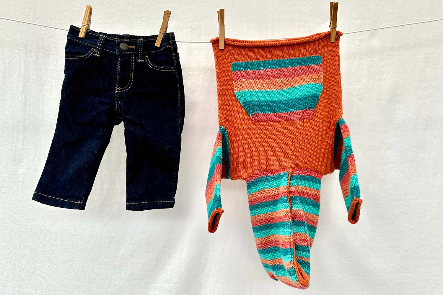 Child's hoodie with striped hood, sleeves, and pocket worked in self-striping yarn, hanging on a clothes line.