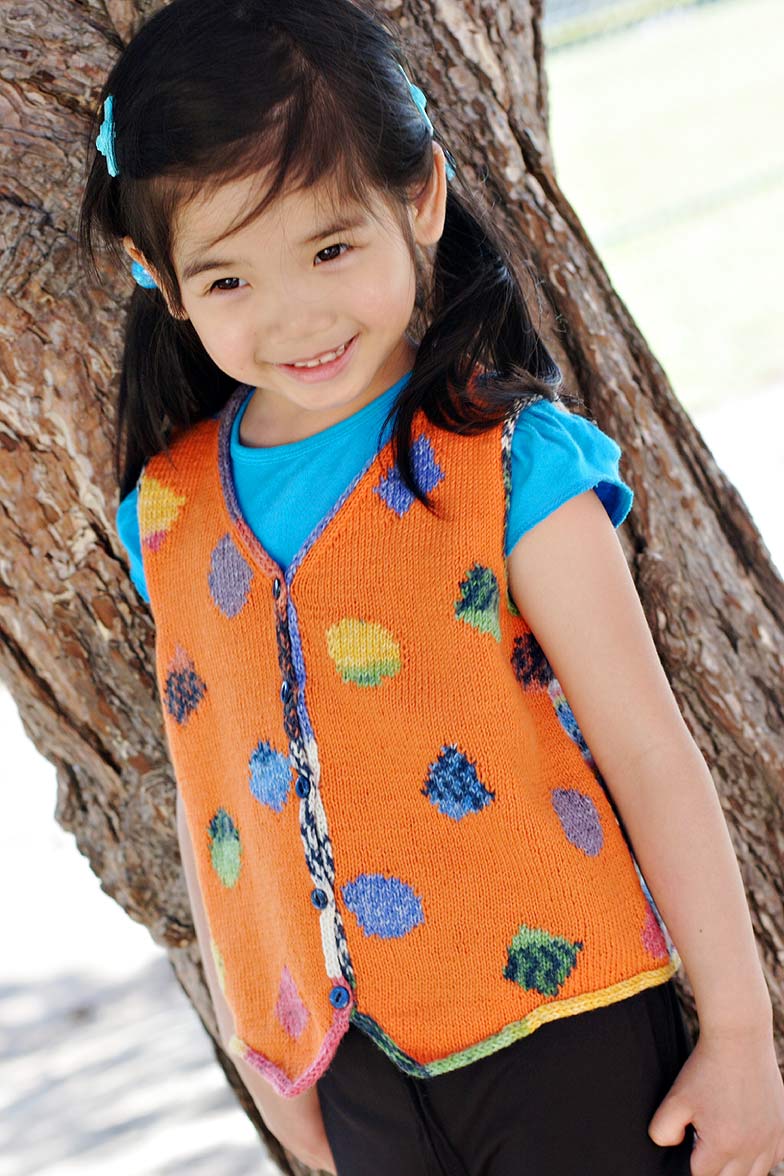 Girl in pigtails wearing orange vest with colourful shapes.