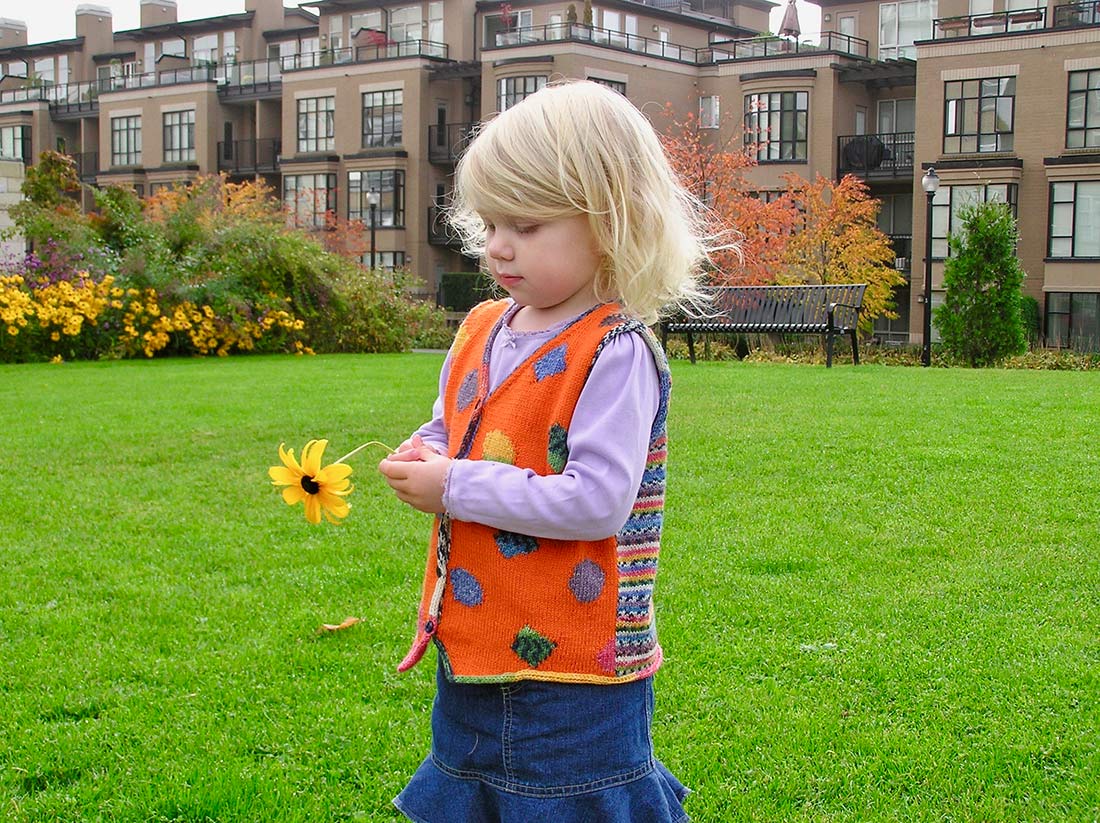Blond girl holding flower showing side view of orange fest with colourful striped back.