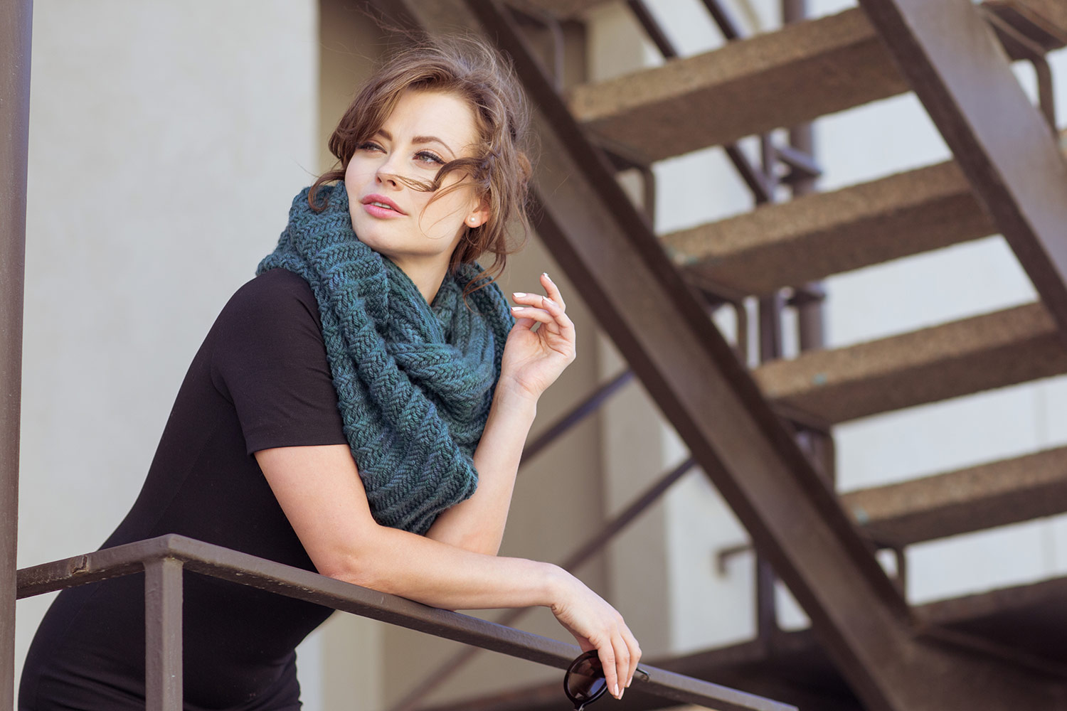 Woman leaning over railing wearing a voluminous cowl around her neck.