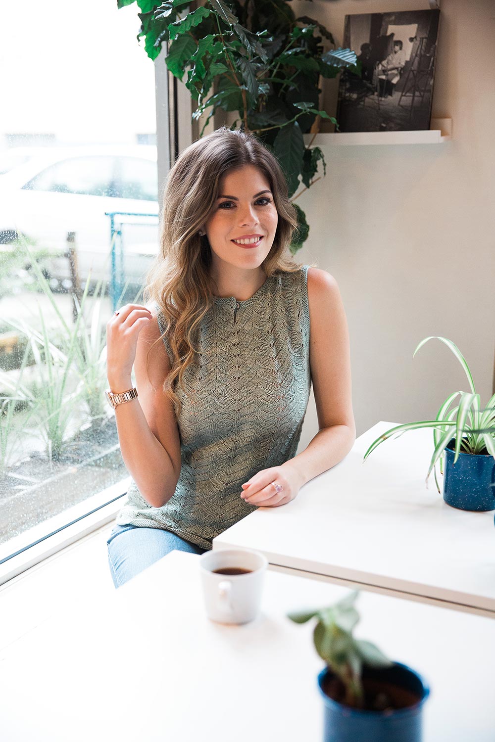 Smiling woman seated at table wearing reversible shell with lace on the front.