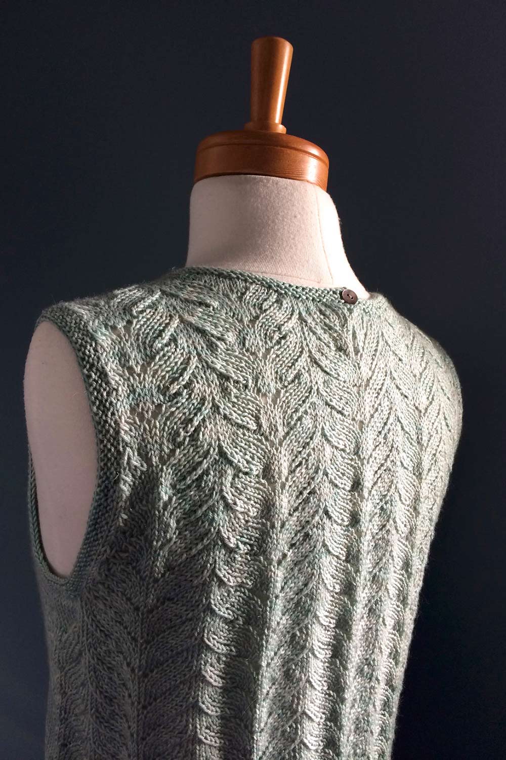 Back view of dress form in moody lighting that picks up the texture of the lace on the back.