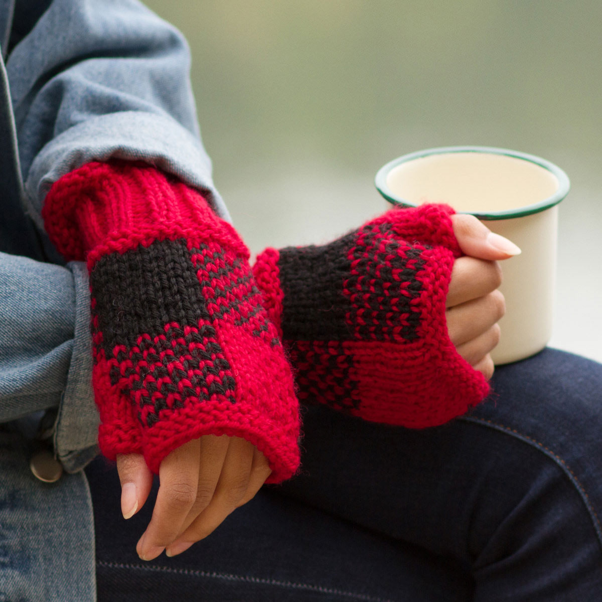 Hands crossed on lap, one hand holding a cut of cocoa and both wearing red and black checkered fingerless mitts.