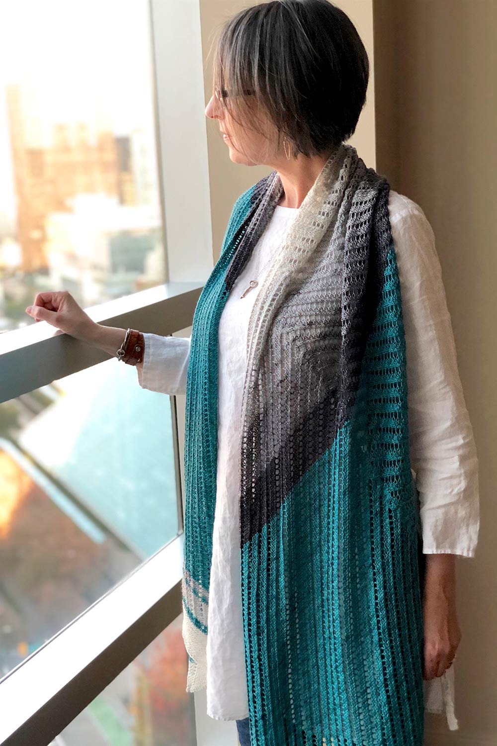 Woman standing at window with rectangular shawl draped around back neck and hanging down the front.