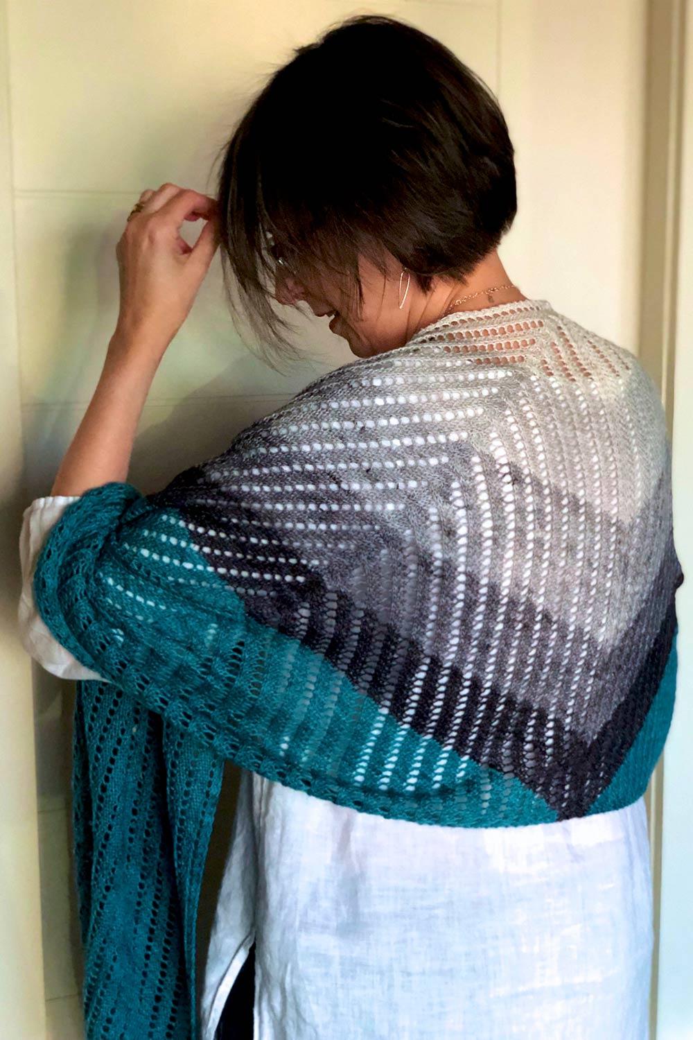 Back view of shawl draped over shoulders showing the triangular shape created by bands of mini skeins before the solid colour is worked on each side to create the rectangular shape.