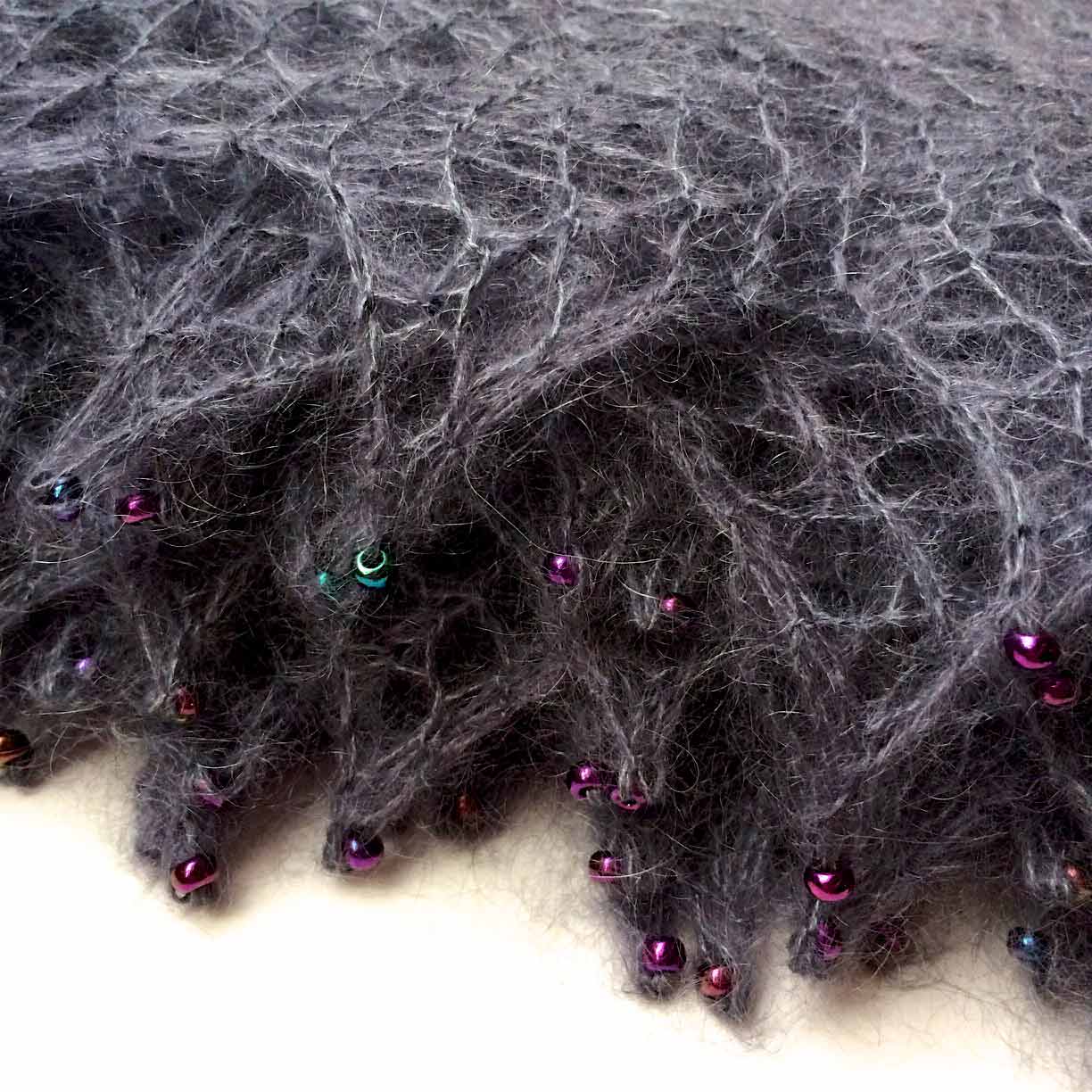 Detail shot of edges of folded up shawl. The lace edging has been hard blocked to create pointy tips, each anointed with a bead.