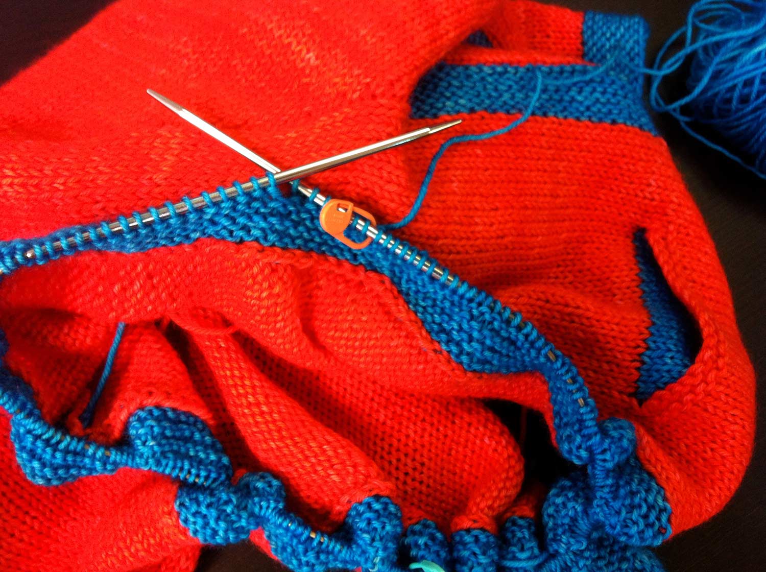 Bright orange project on the needles with bright turquoise garter stitch trim.